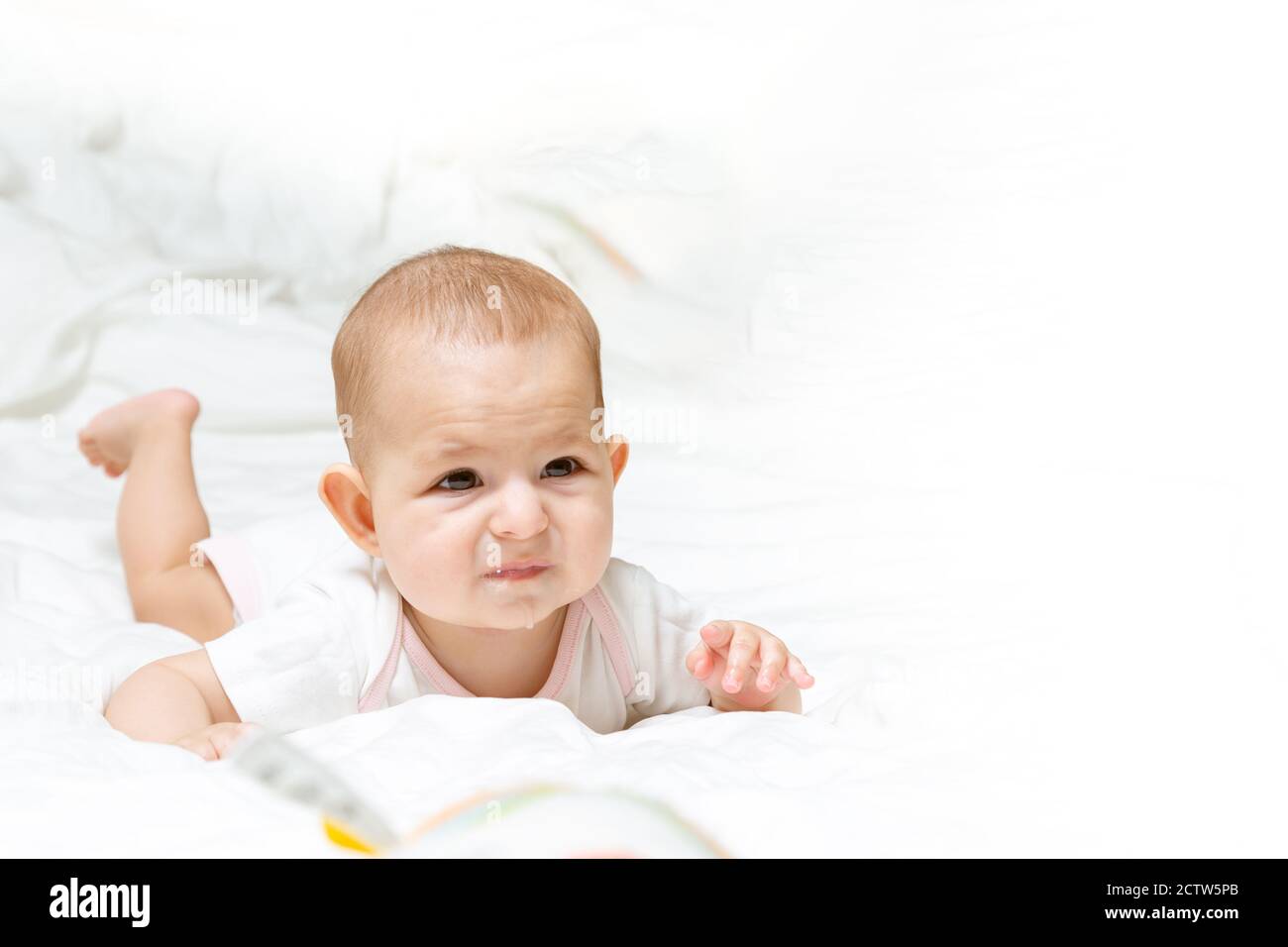Triste Et Decu Bebe Fille En Vetements Blancs Est Couche Sur Un Lit Blanc Et Regarde A Droite Bebe Enfant Allonge Sur Son Ventre Coulure Et Poussee Dentaire Photo Stock Alamy