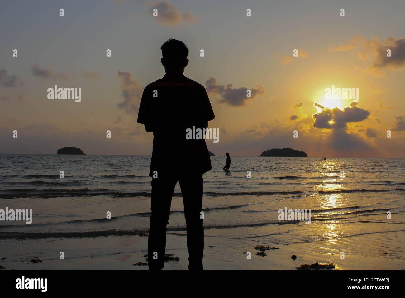 Homme solitaire se tient sur la plage regarde vers la lumière du soleil, marches sur le sable, coucher de soleil, silhouette de personne marchant sur la plage de mer. Banque D'Images