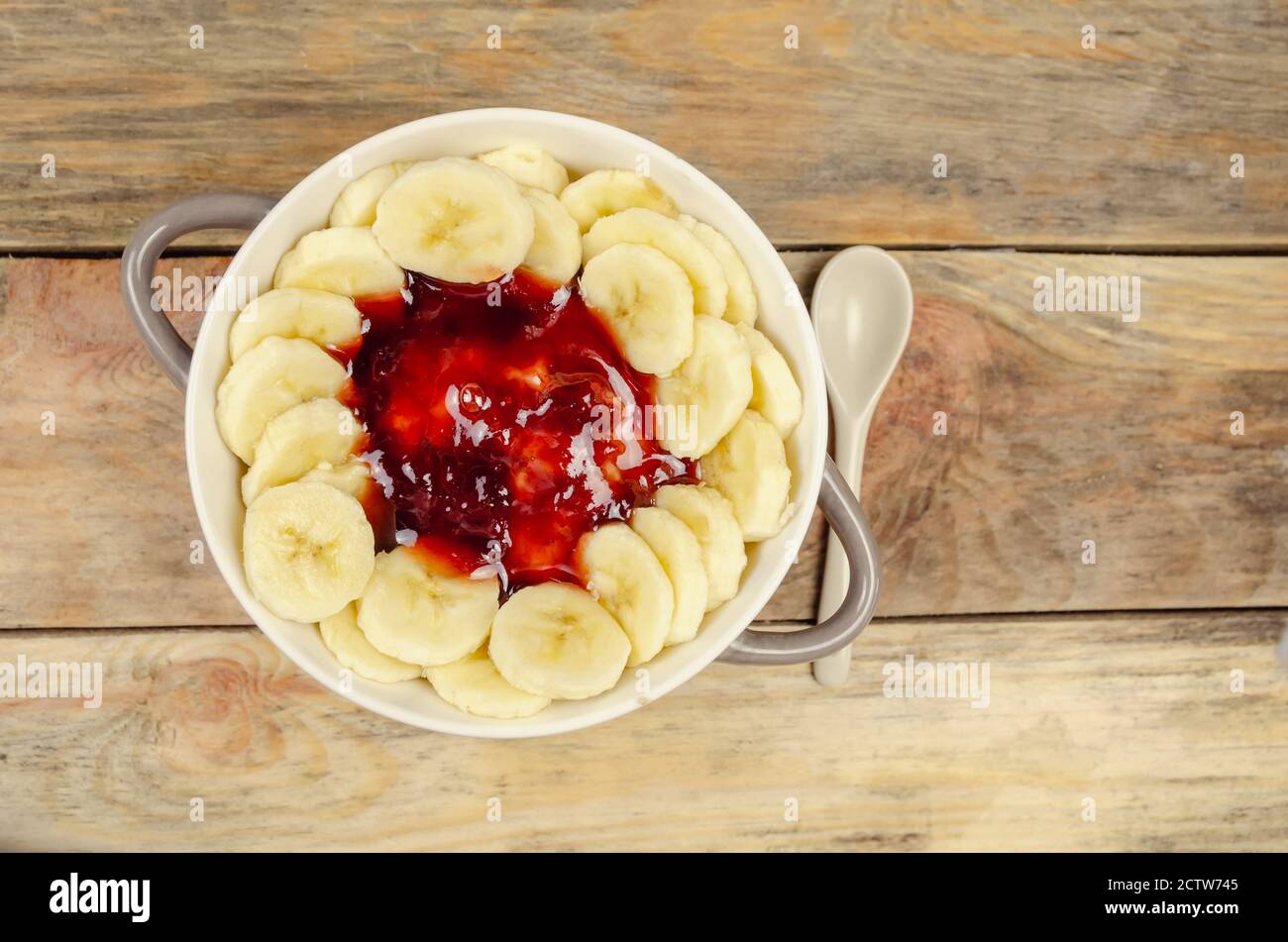 Flocons d'avoine avec confiture et bananes dans une assiette gris blanc avec une cuillère blanche sur fond en bois, vue du dessus, espace de copie. Petit déjeuner sain. Banque D'Images