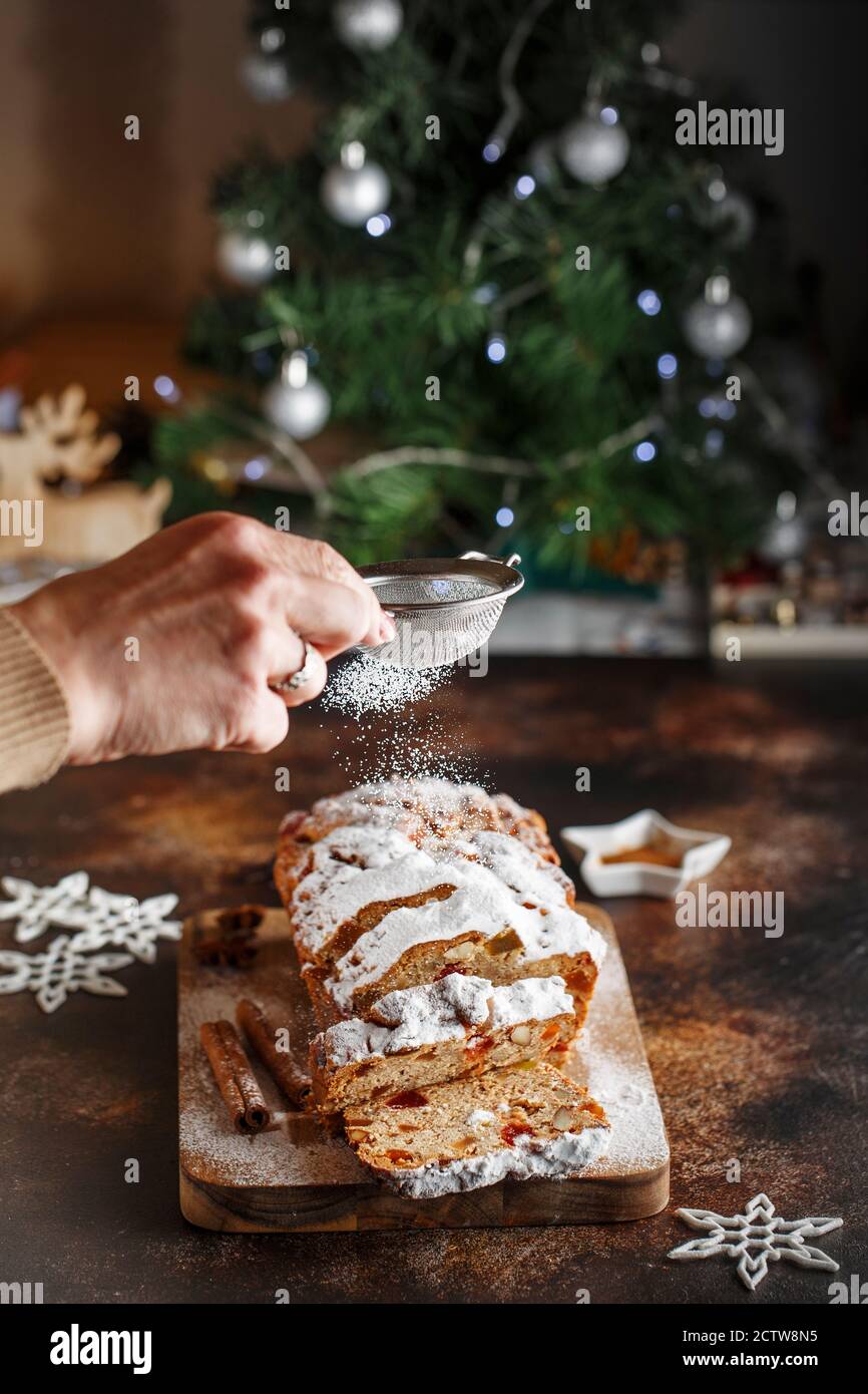 Stollen est un pain aux fruits à coque, aux épices, aux fruits secs ou confits, enrobé de sucre en poudre. Fermez les mains du chef avec le tamis métallique arrosé de la cak Banque D'Images