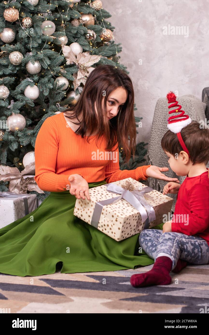 Maman et fils tiennent un cadeau du nouvel an dans un Boîte de fête avec rubans près de l'arbre de Noël 2021 Banque D'Images