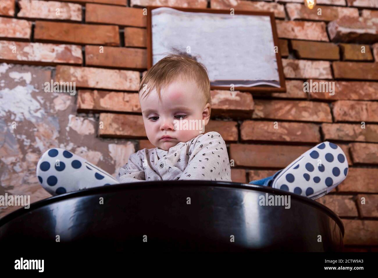 Triste Petit Enfant Est Assis Sur Un Baril De Fer Bebe Garcon Sur Le Fond D Un Mur De Brique Sur Lequel Porte Un Cadre Vide Pour Une Inscription Photo Stock Alamy