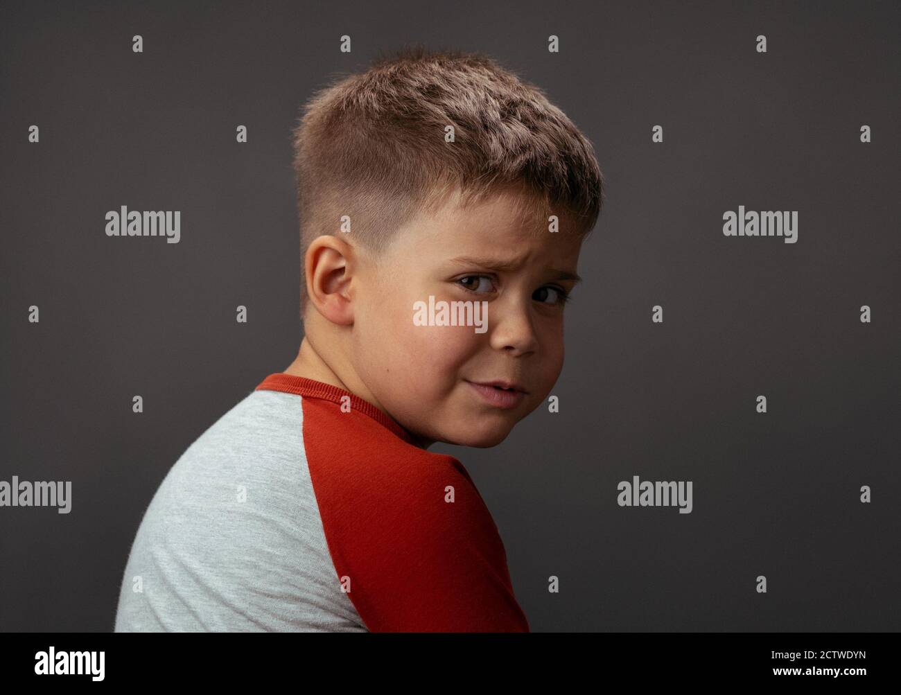L'enfant offensé regarde dans l'appareil photo de derrière son dos. Pleurs en studio sur un fond isolé. Photo de haute qualité Banque D'Images