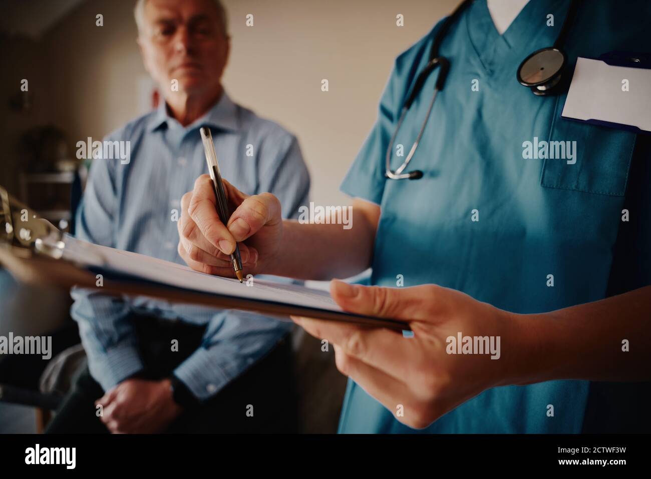 Gros plan des mains d'une jeune femme médecin écrivant médical notes sur le presse-papiers avec le patient senior en arrière-plan Banque D'Images