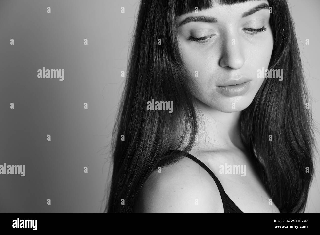Gros plan portrait en studio d'une jolie femme brunette dans un haut à bandoulière spaghetti noir, regardant son épaule, à moitié retournée, contre un backgro gris Uni Banque D'Images