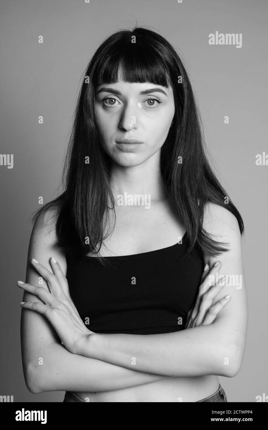 Portrait studio d'une jolie femme brunette dans un haut de bande spaghetti noir, regardant sérieusement l'appareil photo, debout sur un fond gris Uni Banque D'Images