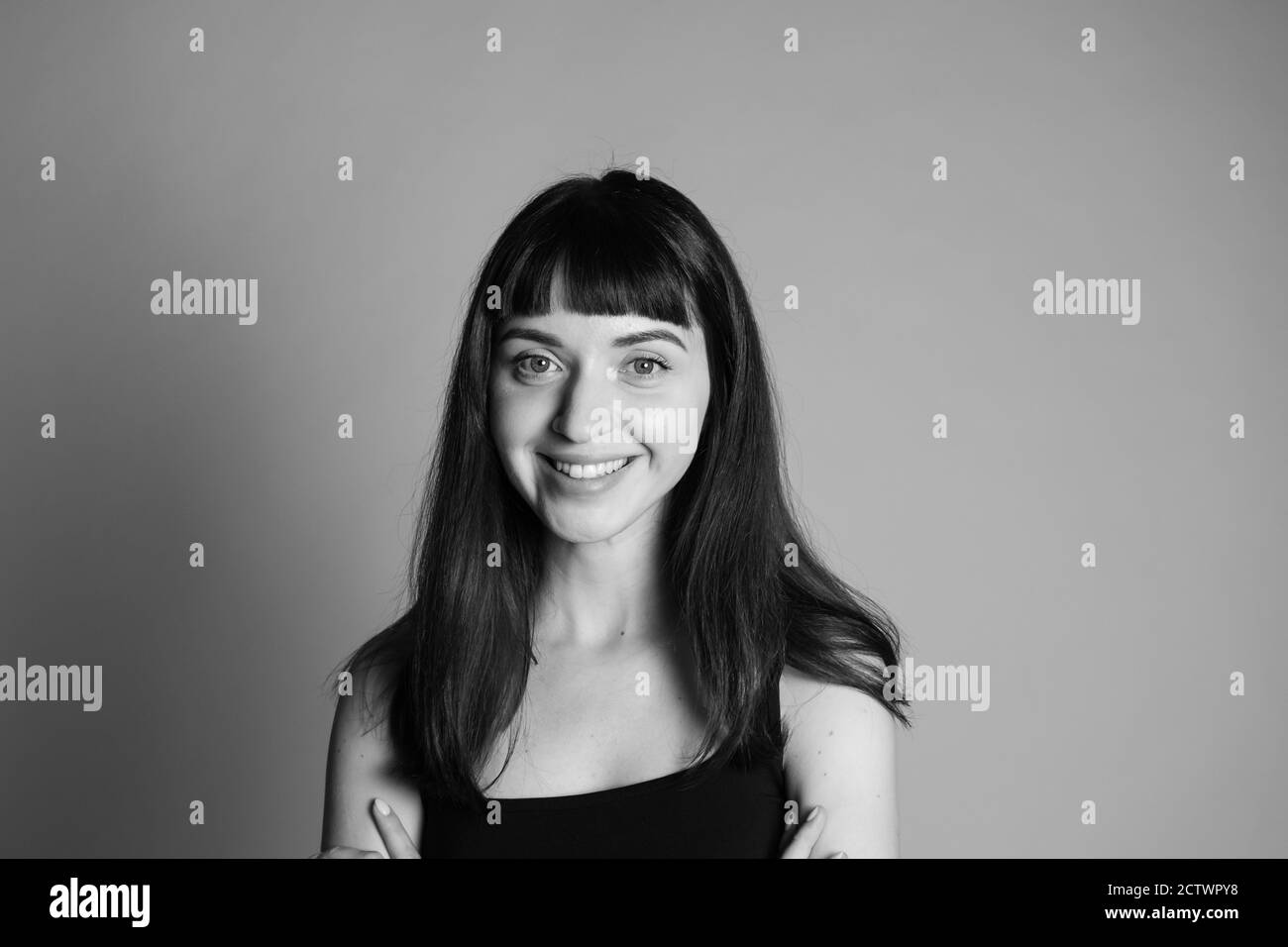 Portrait studio d'une femme souriante, portant un haut à bandoulière spaghetti, regardant l'appareil photo, sur un fond gris Uni Banque D'Images