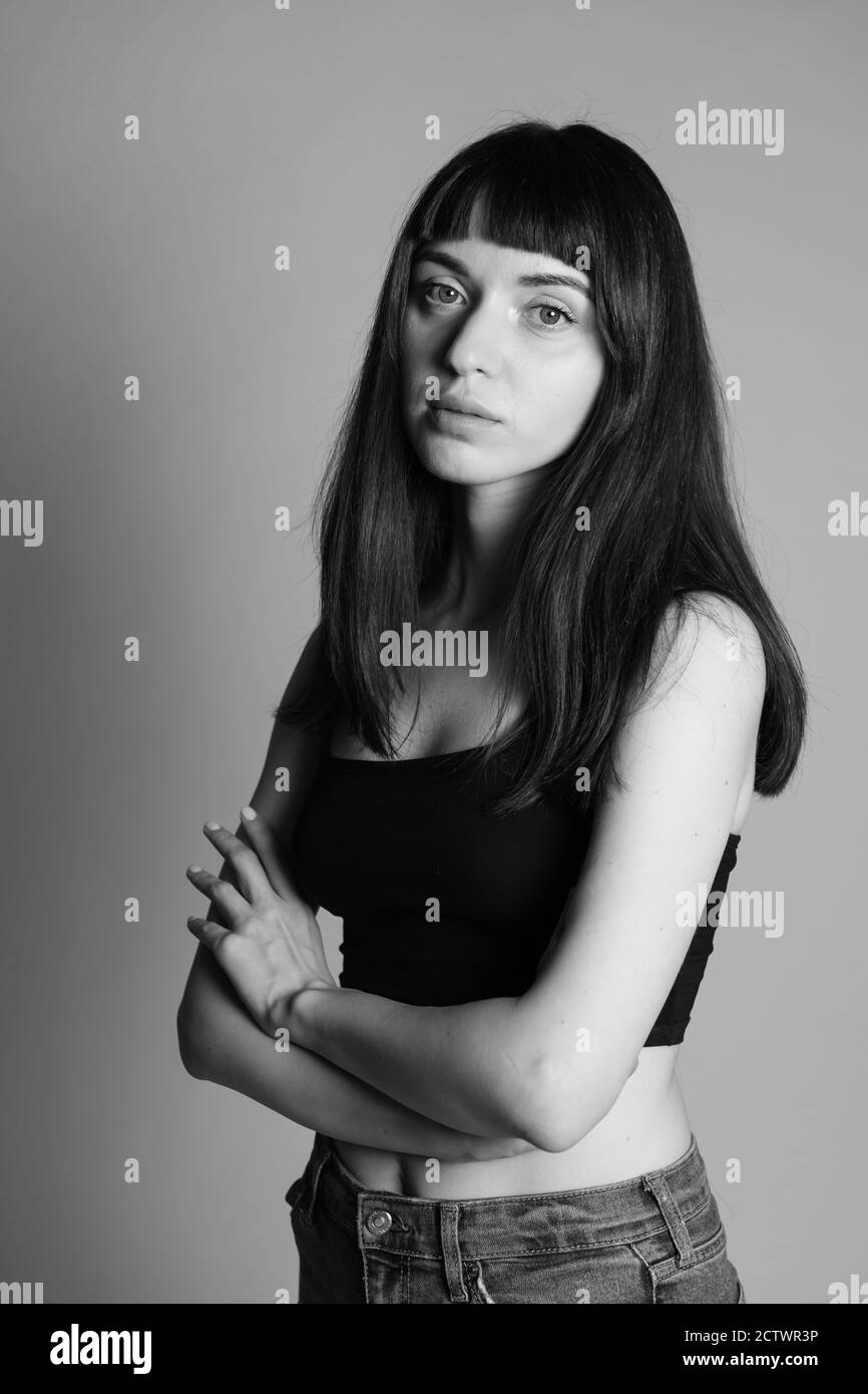 Portrait studio d'une jolie femme brunette dans un haut de bande spaghetti noir, regardant sérieusement l'appareil photo, debout sur un fond gris Uni Banque D'Images