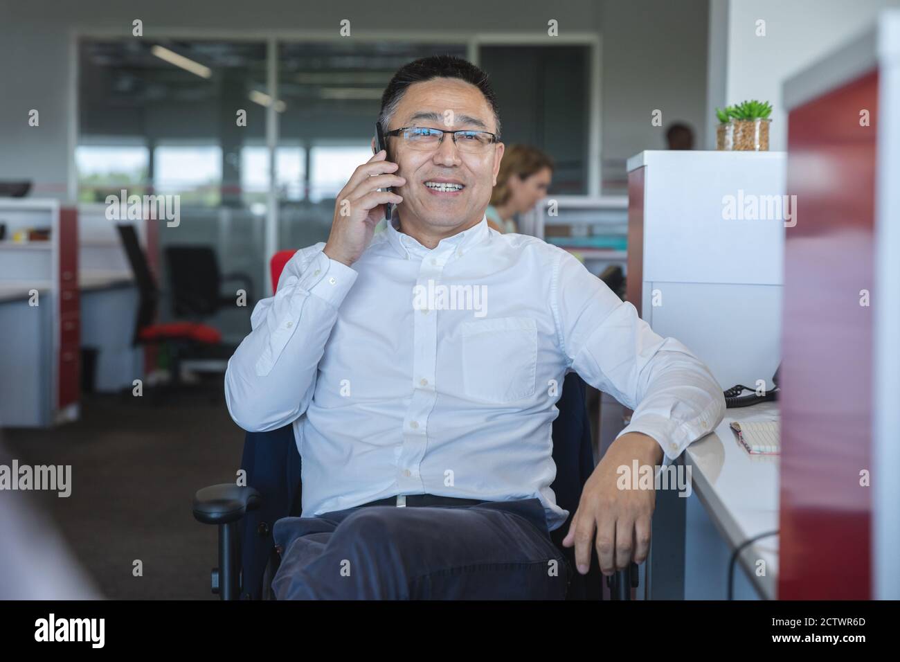 Élégant décontracté asiatique homme créatif d'affaires portant des lunettes assis à un bureau souriant, parlant sur un smartphone. Professionnel de la création avec Banque D'Images