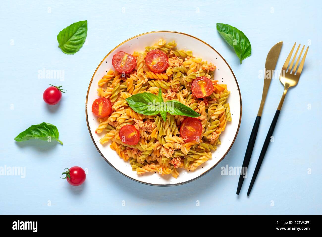 Fusilli - pâtes italiennes classiques de blé dur avec viande de poulet, tomates cerises, basilic dans une sauce tomate dans un bol blanc sur une table en bois bleu Banque D'Images