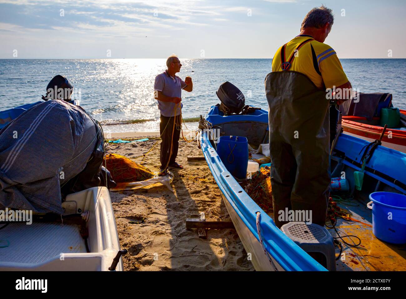 Deux pêcheurs sur la plage, l'un dans le bateau et l'autre à côté du bateau, empilent le filet de poisson pour la prochaine pêche à la ligne. Banque D'Images