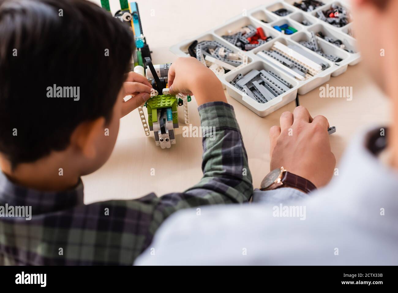 Vue arrière d'un enseignant assis près d'un robot de modélisation d'un écolier asiatique à la table dans l'école de la tige Banque D'Images