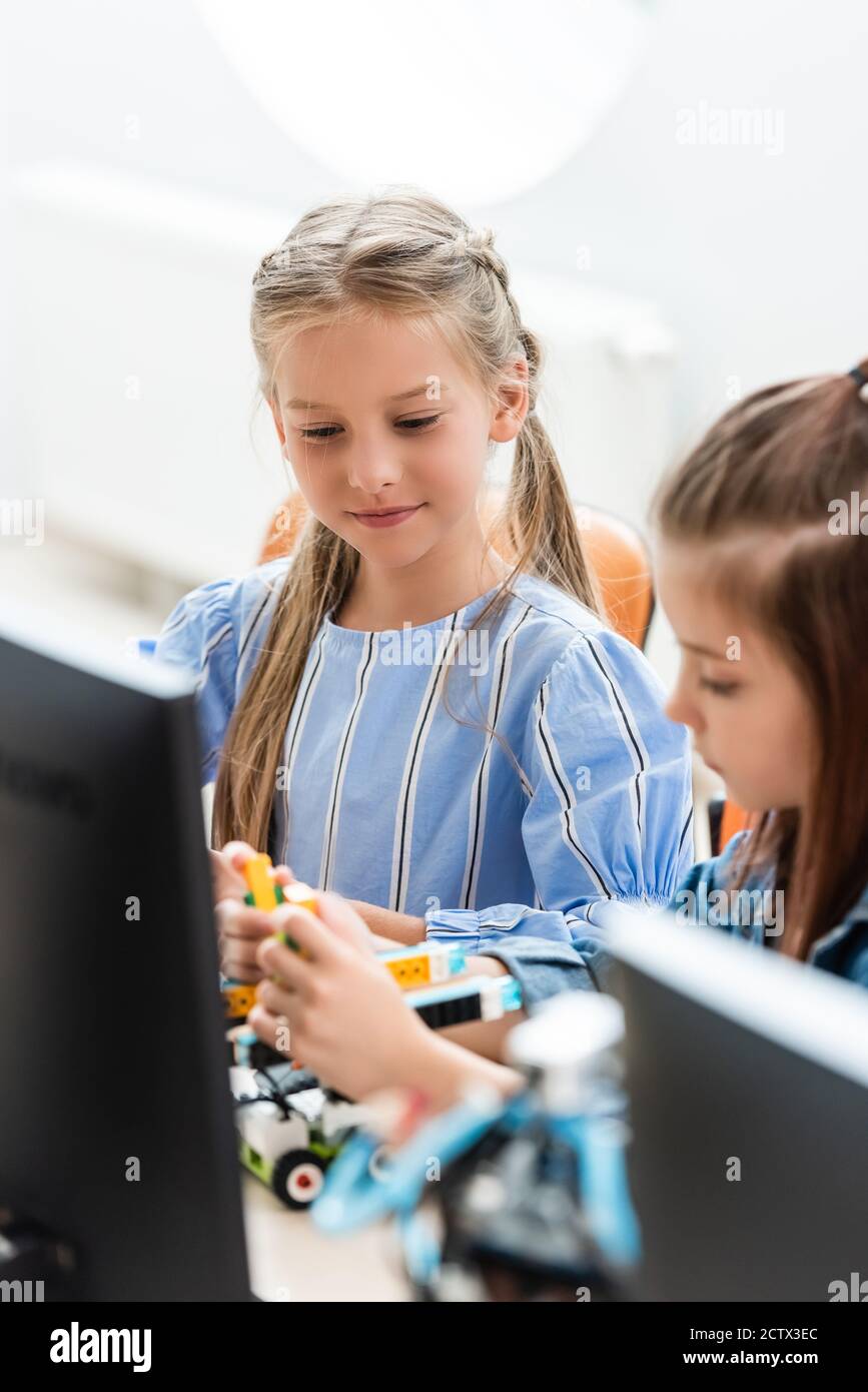 Objectif sélectif des écolières programmant le robot près de l'ordinateur à l'école Banque D'Images