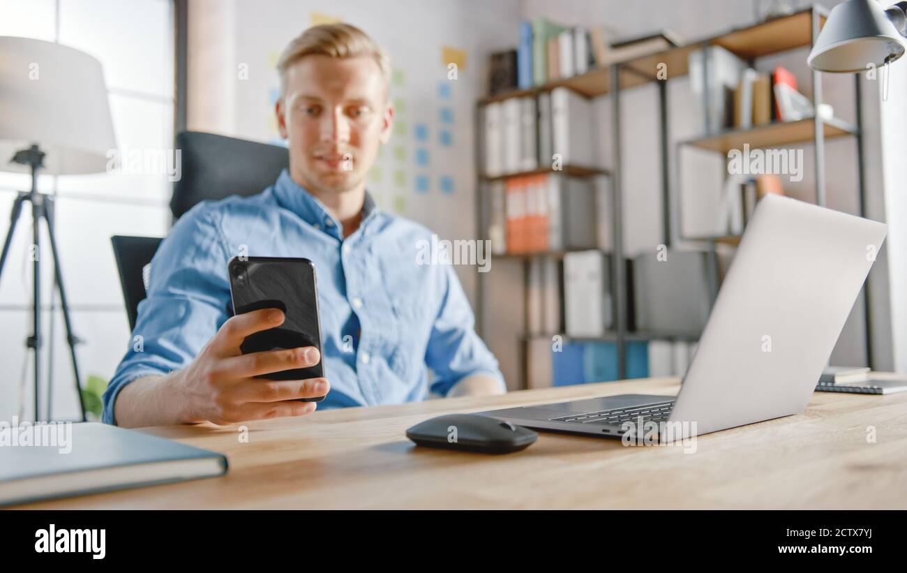 Homme d'affaires assis à son bureau travaille sur l'ordinateur de bureau dans l'élégant bureau, choisit et commence à utiliser le smartphone, utilise l'application de médias sociaux, l'envoi par e-mail Banque D'Images