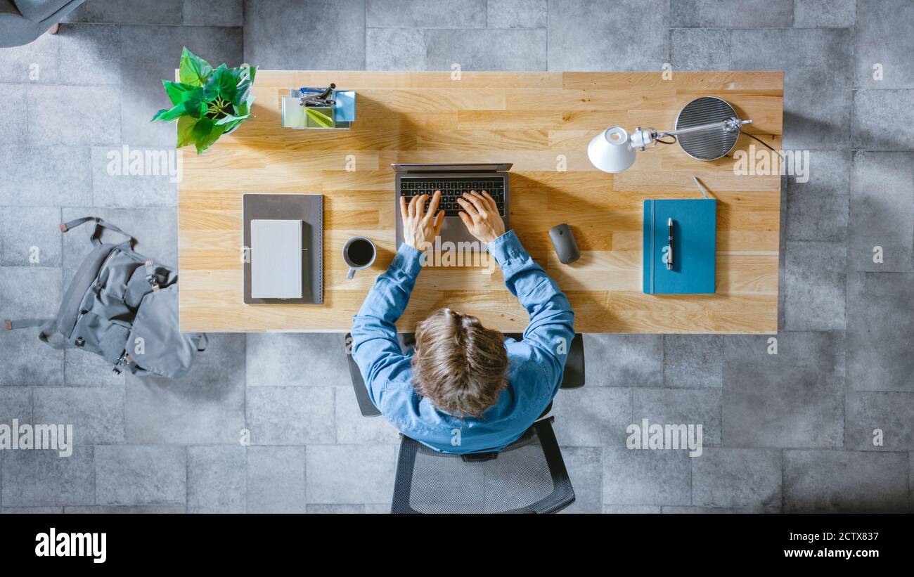 Vue de dessus photo: Homme d'affaires assis au bureau en bois travaille sur un ordinateur portable dans son bureau à domicile. Il tape, écrit des e-mails, surfe l'Internet, des dessins Banque D'Images