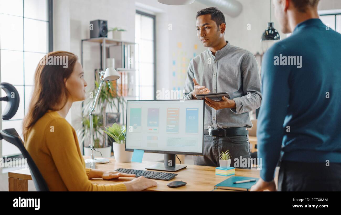 Trois développeurs de logiciels mobiles travaillent sur un ordinateur de bureau, ils discutent de la conception d'applications de smartphone utiliser la tablette numérique à écran tactile. Moderne et élégant Banque D'Images