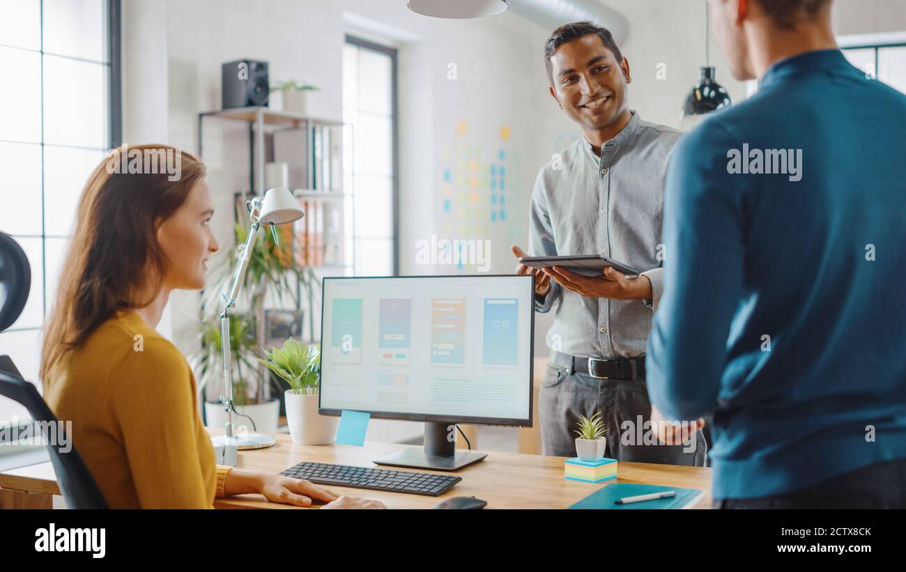 Trois développeurs de logiciels mobiles travaillent sur un ordinateur de bureau, ils discutent de la conception d'applications de smartphone utiliser la tablette numérique à écran tactile. Moderne et élégant Banque D'Images