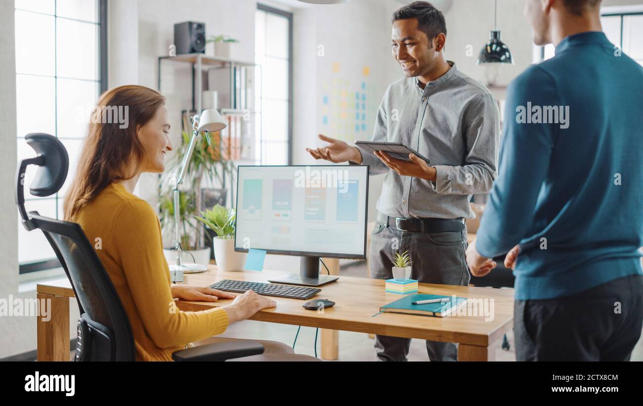Trois développeurs de logiciels mobiles travaillent sur un ordinateur de bureau, ils discutent de la conception d'applications de smartphone utiliser la tablette numérique à écran tactile. Moderne et élégant Banque D'Images