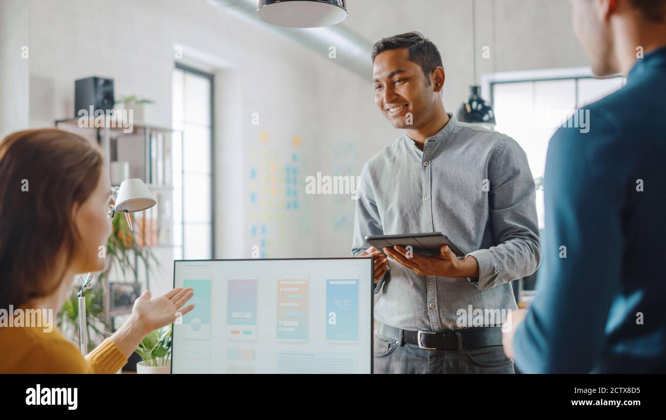 Trois développeurs de logiciels mobiles travaillent sur un ordinateur de bureau, ils discutent de la conception d'applications de smartphone utiliser la tablette numérique à écran tactile. Moderne et élégant Banque D'Images
