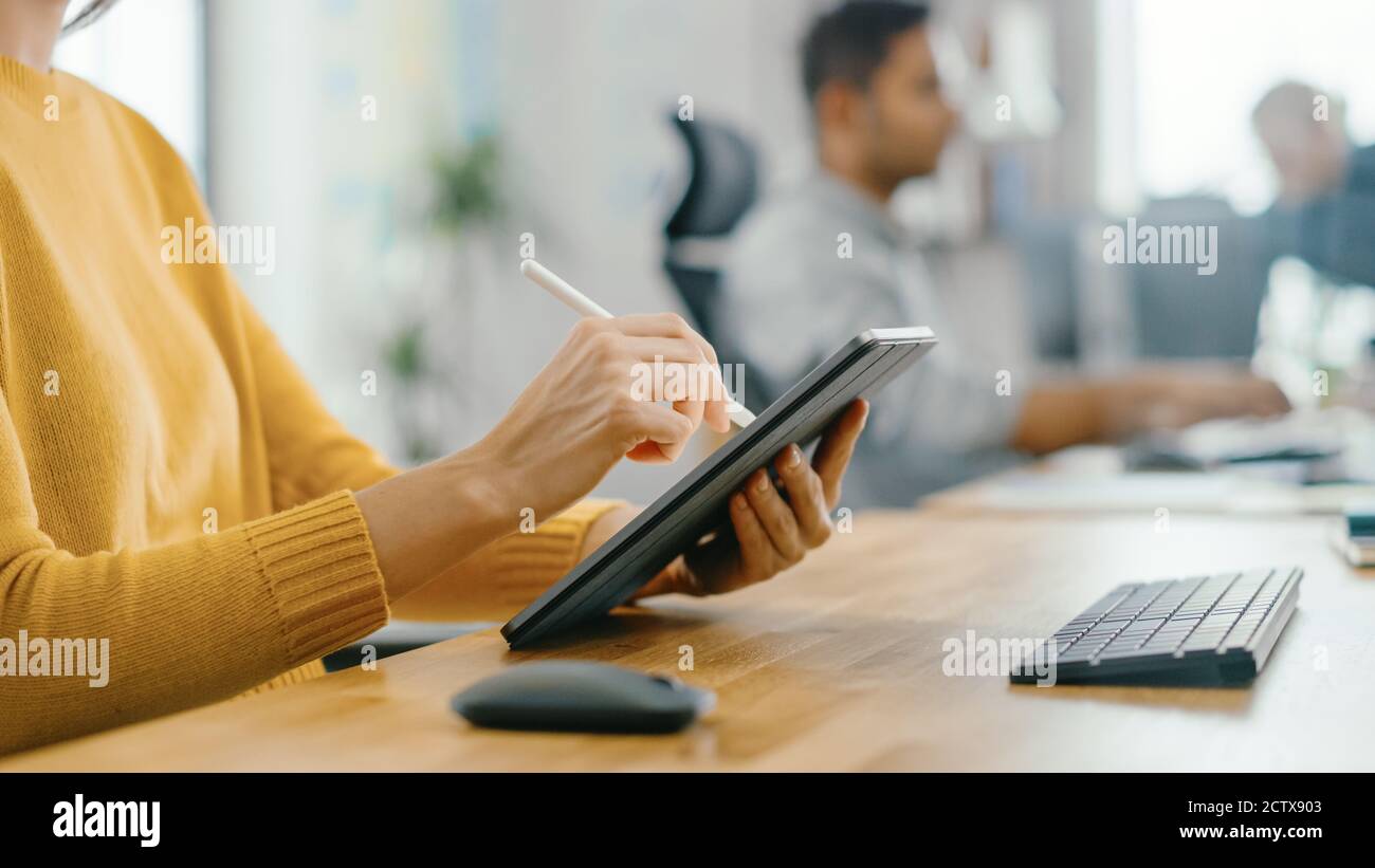 Anonyme jeune femme assise à son bureau elle est dessin, écriture et utilisation de stylo avec ordinateur de tablette numérique. Concentrez-vous sur vos mains avec le stylet. Bureau lumineux Banque D'Images