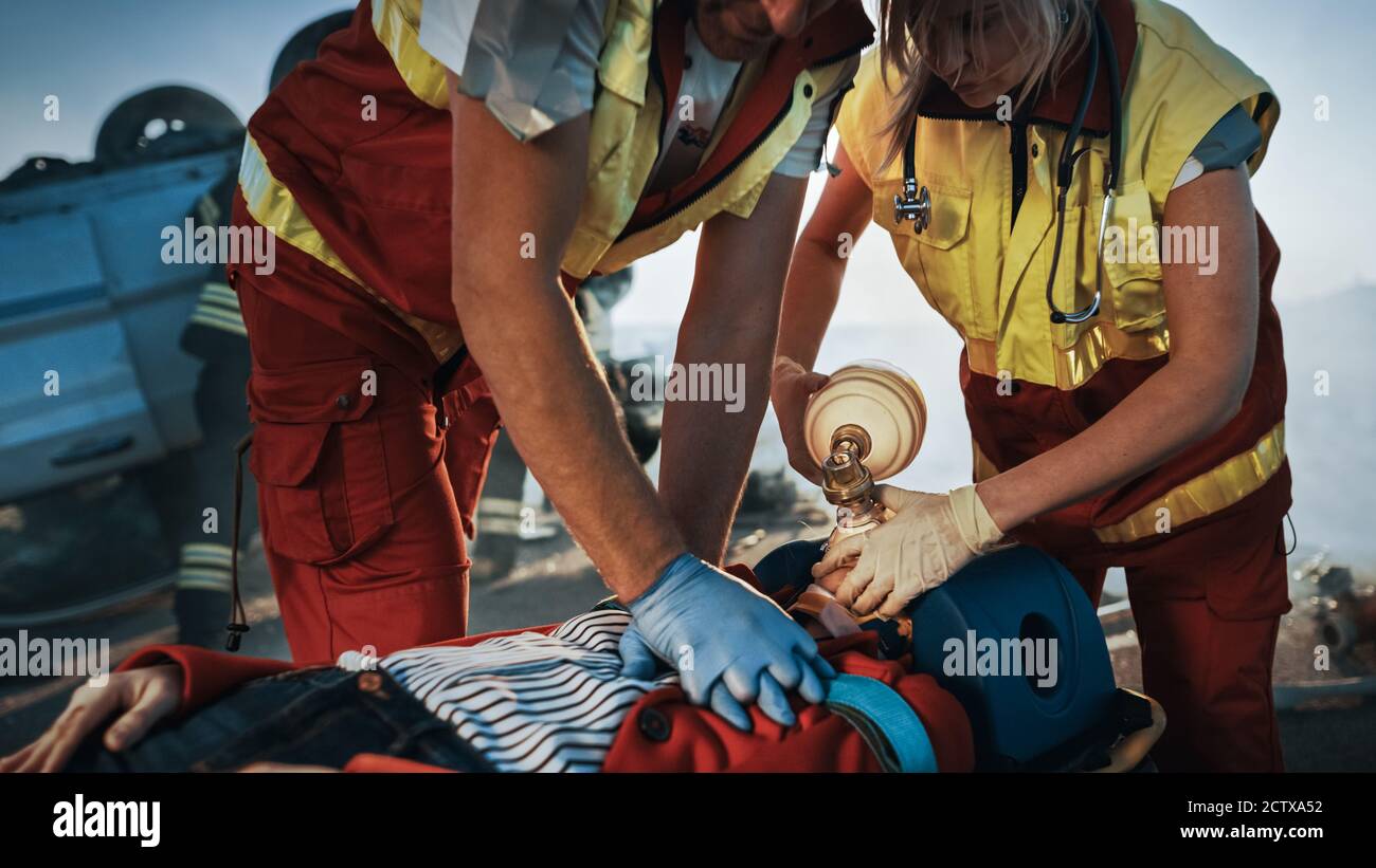 Sur la scène d'accident de la circulation automobile : les ambulanciers paramédicaux sauvant la vie d'une victime femelle qui est allongé sur des brancards. Ils appliquent le masque d'oxygène, font Banque D'Images