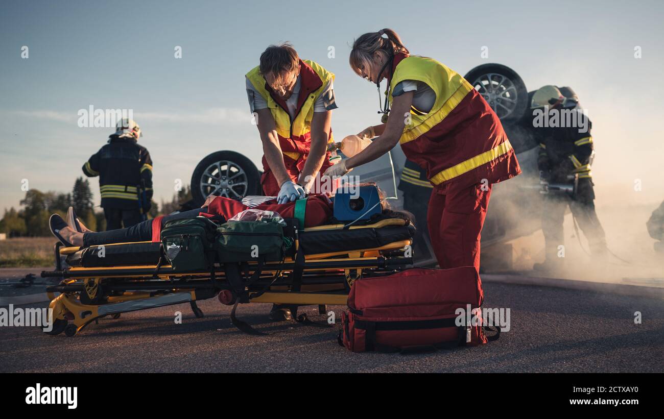 Sur la scène d'accident de la circulation automobile : les ambulanciers paramédicaux sauvant la vie d'une victime femelle qui est allongé sur des brancards. Ils appliquent le masque d'oxygène, font Banque D'Images