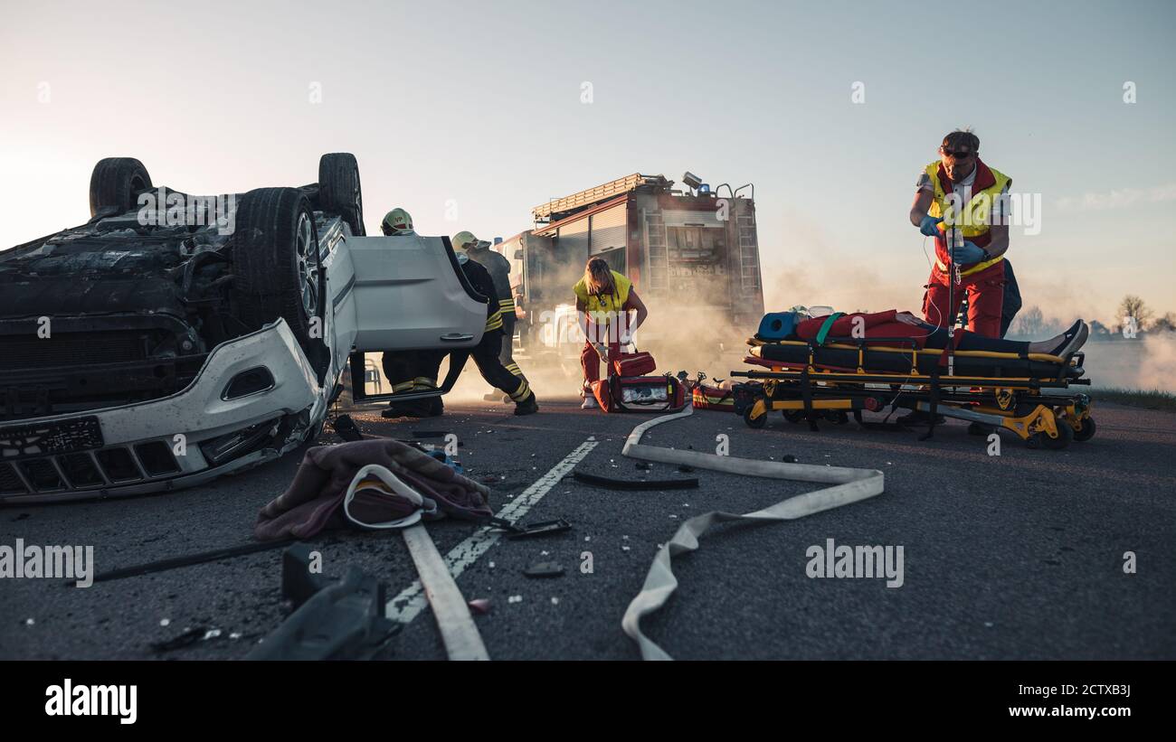 Les ambulanciers paramédicaux et les pompiers arrivent sur la scène des accidents de la route. Professionnels de secours la victime blessée piégée dans le véhicule en retournement par Banque D'Images