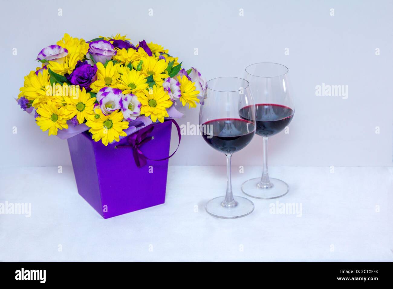 Magnifique bouquet coloré lumineux avec chrysanthème jaune et eustoma pourpre fleurs dans un boxet vin rouge dans un verre arrière-plan blanc Banque D'Images