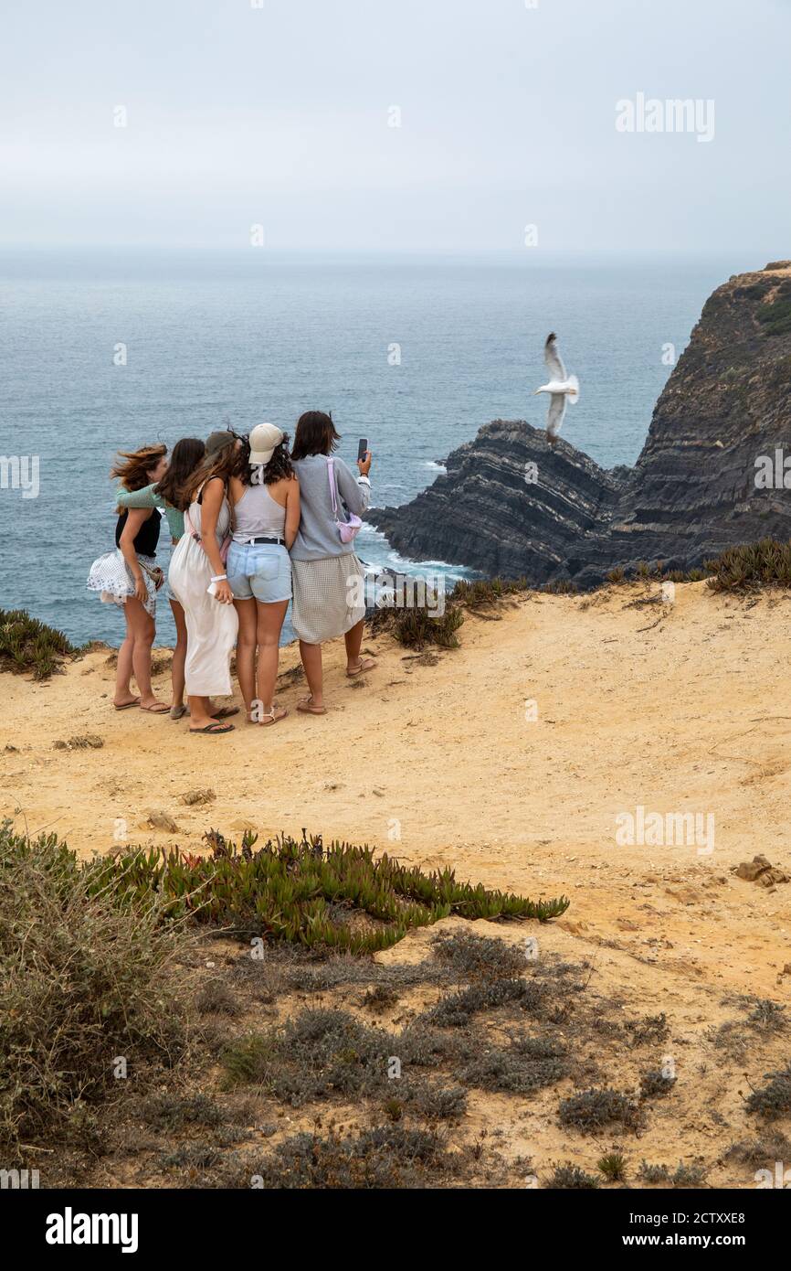 Groupe de filles prenant des selfies près d'une falaise au bord de la mer, au cap Sardão, Alentejo, Portugal. Banque D'Images
