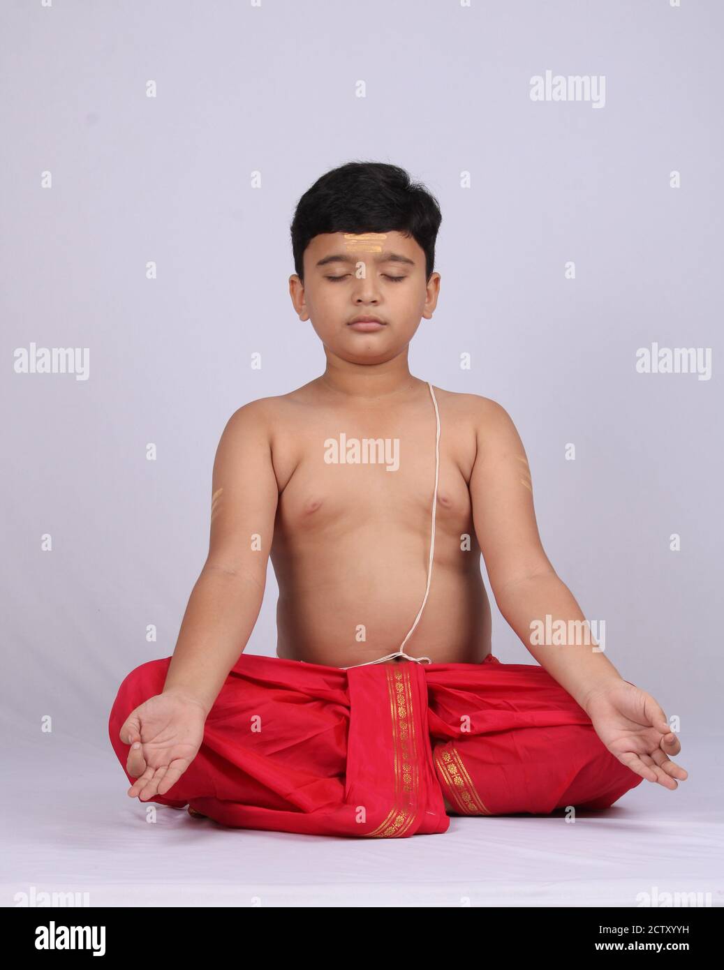 Un jeune enfant indien mignon faisant du yoga sur fond blanc, portant un dhoti. Posture de méditation. Banque D'Images