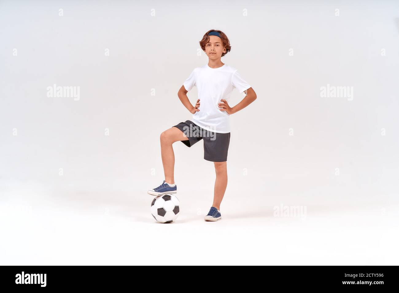 Joueur de football. Prise de vue en longueur d'un adolescent heureux avec ballon de football regardant l'appareil photo et souriant tout en se tenant isolé sur fond gris Banque D'Images