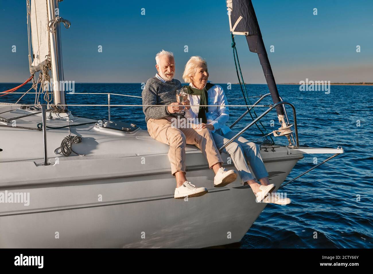 Célébration de l'anniversaire de mariage. Joyeux couple senior qui boit du vin ou du champagne et rit tout en s'asseyant sur un voilier ou un pont de yacht flottant dans un Banque D'Images