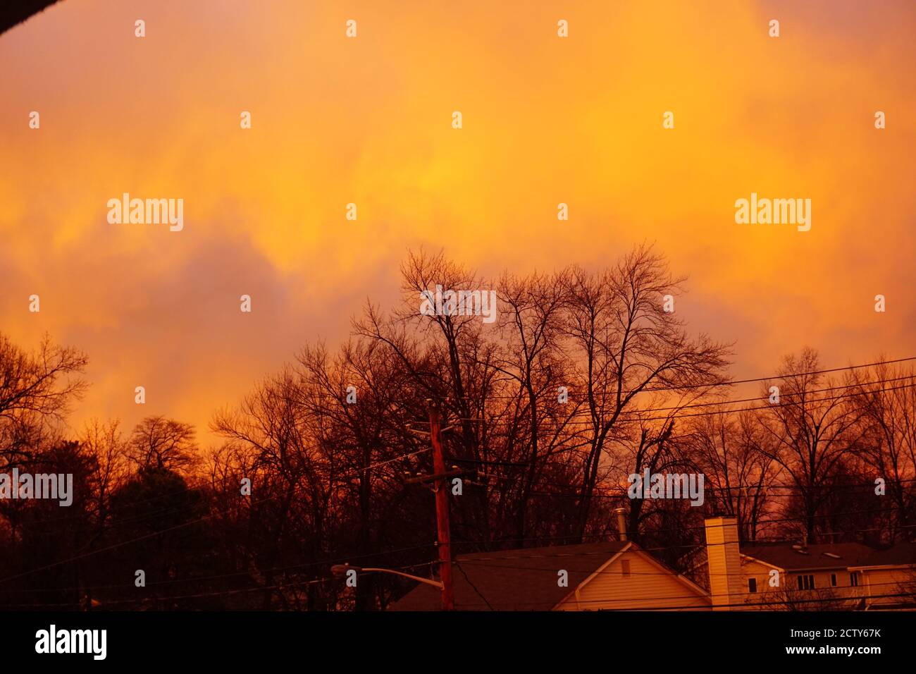 Un ciel violet, jaune et orange avec des nuages et un coucher de soleil au-dessus des maisons, des lignes électriques et des feux de rue vus d'un pont dans la banlieue. Banque D'Images