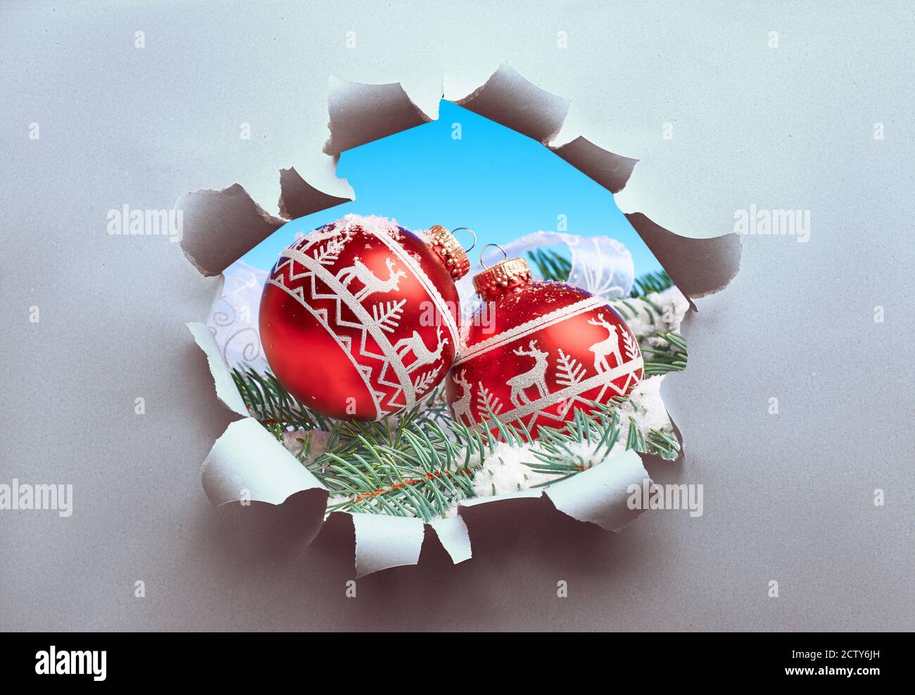 Breloques de Noël rouges sur brindilles de sapin visibles à travers le trou déchiré dans le papier artisanal. Concept créatif de la saison de Noël soudaine. Banque D'Images