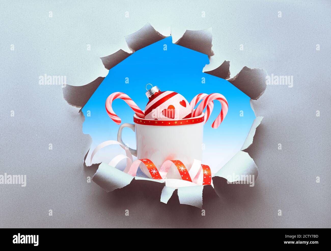 Boule de Noël et Cannes en sucre dans une tasse visible à travers le trou déchiré dans le papier artisanal. Concept créatif de la saison de Noël soudaine. Banque D'Images