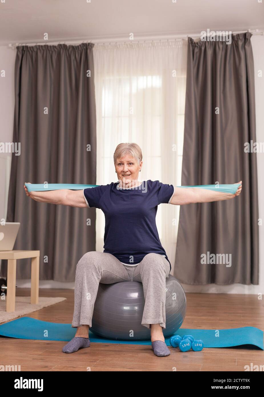 Femme à la retraite avec un esprit sain, assis sur un ballon d'équilibre et  de l'entraînement avec une bande élastique. Personne âgée pensionné en  ligne entraînement à l'exercice sur Internet à la