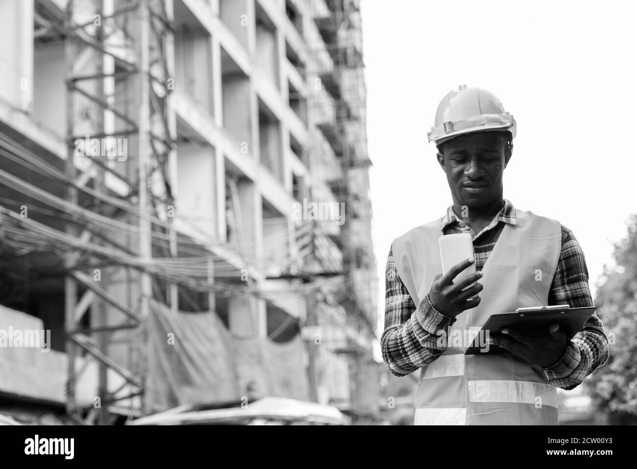 Young black African man construction worker lecture le presse-papiers en maintenant le téléphone mobile au chantier Banque D'Images