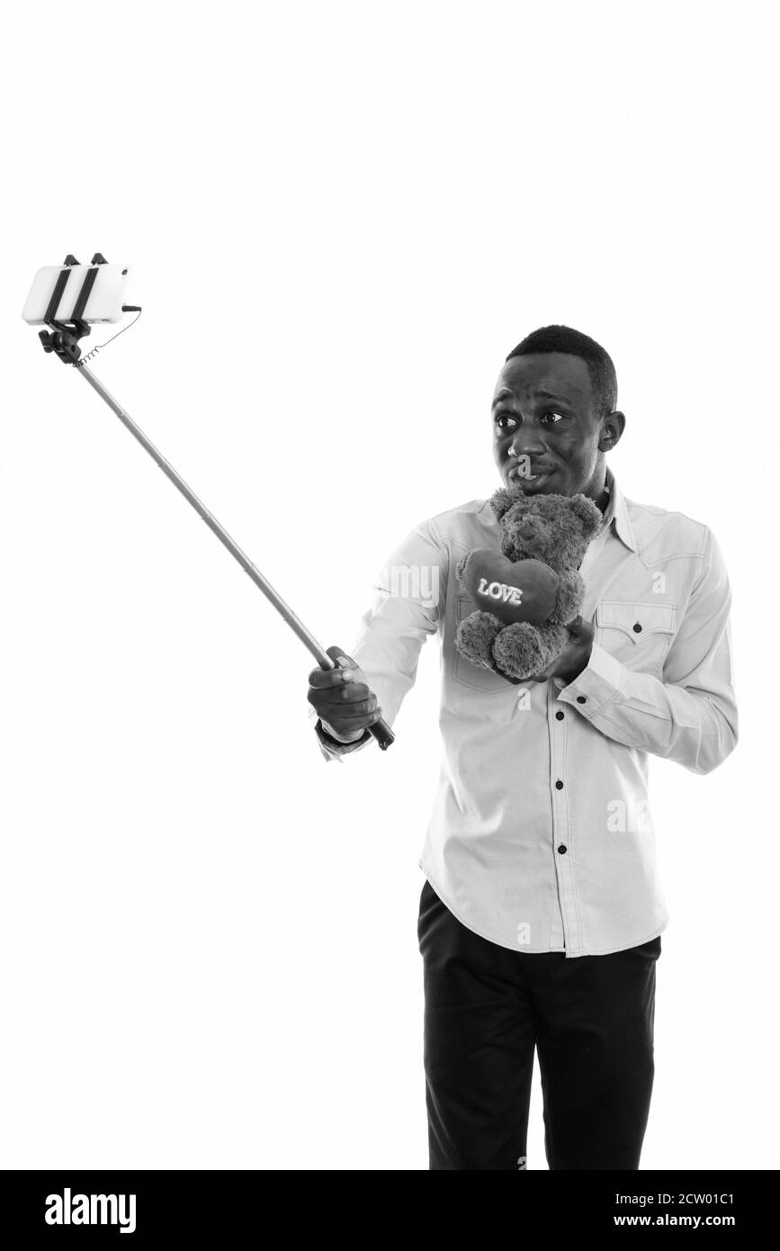 Jeune homme africain tenant un ours en peluche tout en prenant le selfie avec téléphone portable sur clé pour selfie Banque D'Images