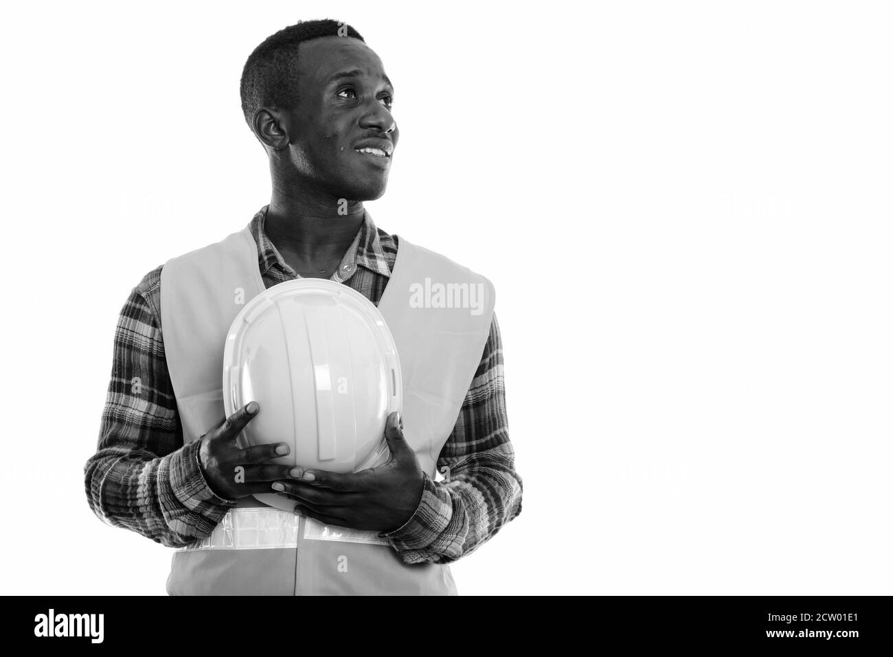 Studio shot of young happy black African man construction worker smiling et pensant alors que holding hard hat Banque D'Images