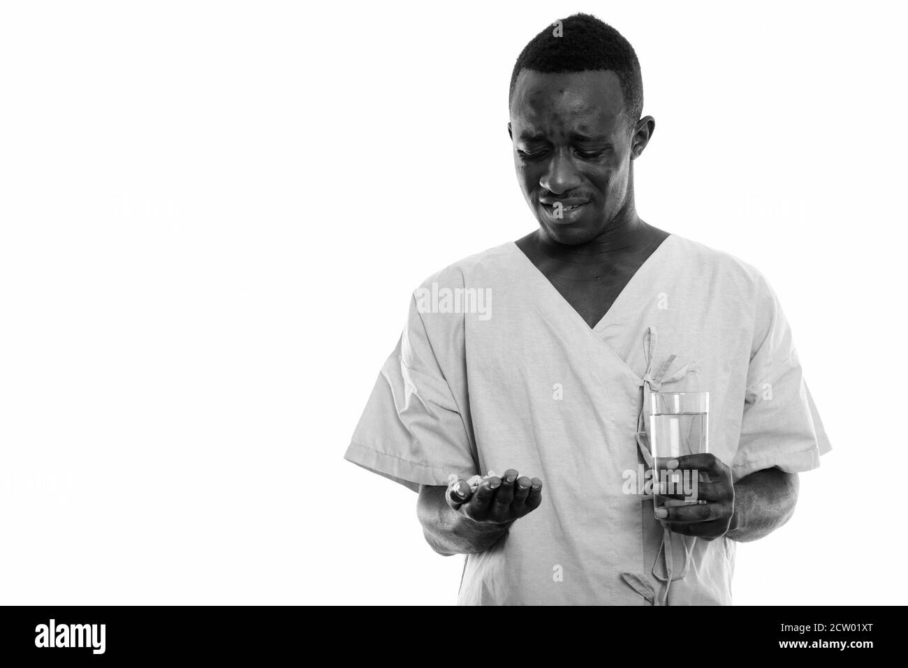 Portrait de jeune homme Africain noir dégoûté à patient et comprimés de vitamines holding glass of water Banque D'Images
