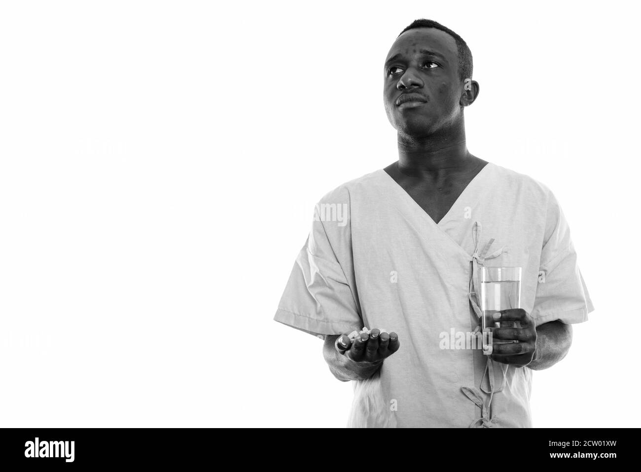 Portrait de jeune homme de l'Afrique noire de la pensée du patient tout en maintenant les comprimés de vitamines et de verre d'eau Banque D'Images