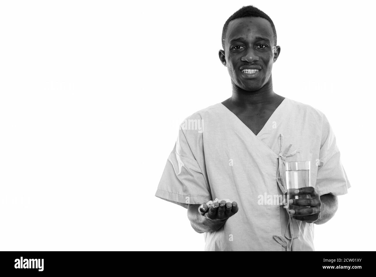 Studio shot of young happy black African man smiling patient tout en maintenant les comprimés de vitamines et de verre d'eau Banque D'Images