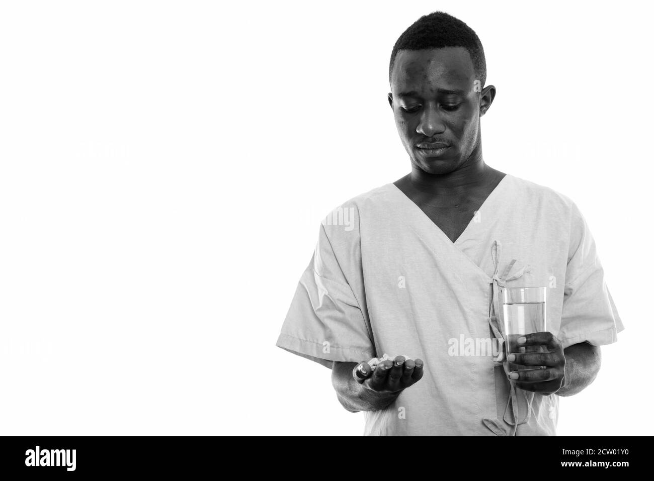 Studio shot of young black African man patient comprimés de vitamine et holding glass of water Banque D'Images