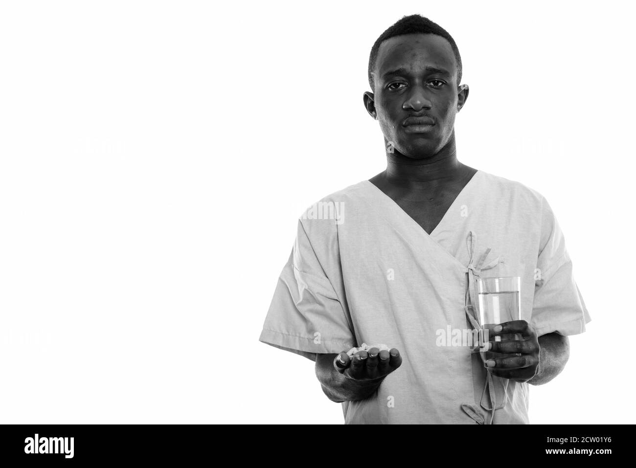 Studio shot of young black African man holding patient comprimés de vitamines et de verre d'eau Banque D'Images