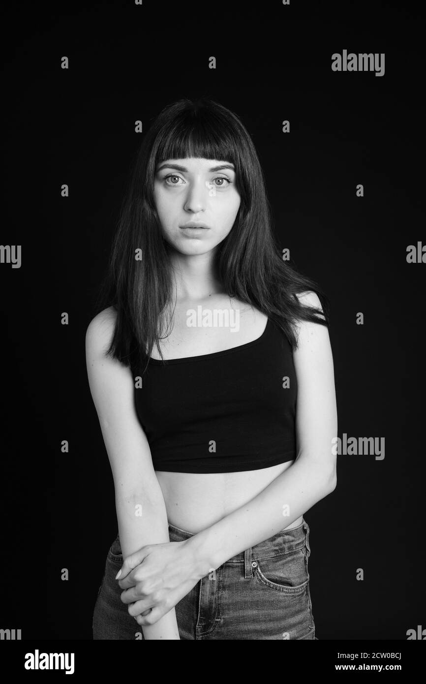 Studio portrait d'une jolie femme brune dans un haut de la bande noire spaghetti, debout avec des bras croisés, regardant l'appareil photo, debout contre une plaine Banque D'Images