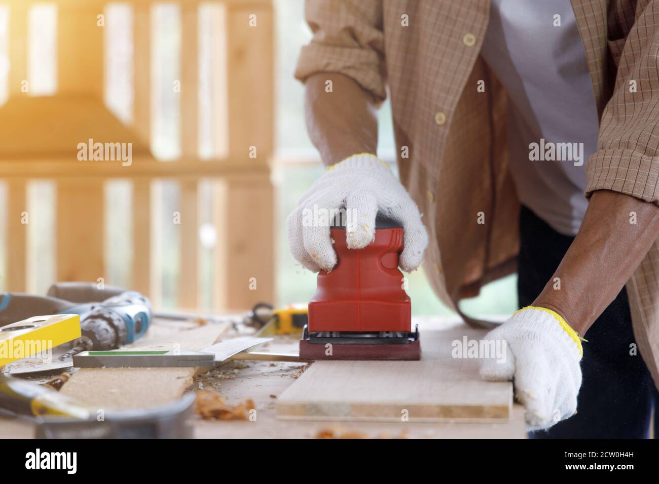 L'homme ancien utilise une fraiseuse électrique rouge pour lisser la surface du panneau en bois dans l'atelier de menuiserie. Banque D'Images