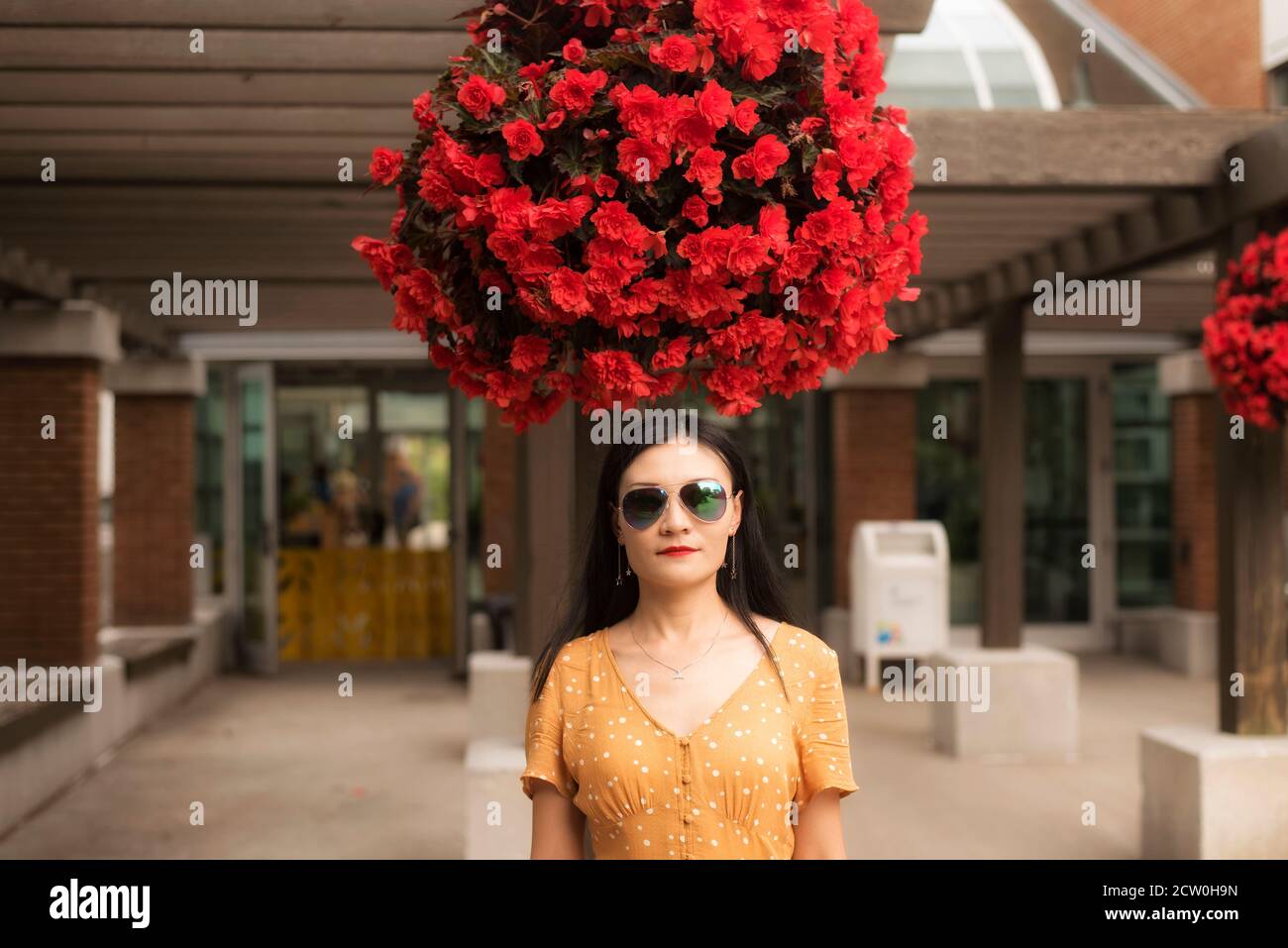 Une chinoise debout sous un grand pot suspendu de begonias rouges à l'entrée du jardin bontanique de montréal, Québec canada. Banque D'Images