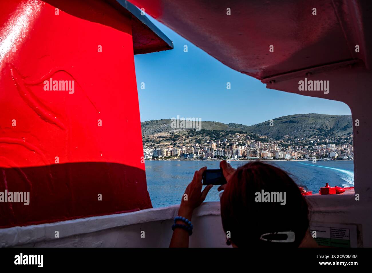 Vue sur la mer Adriatique de la ville et station de Saranda, Albanie, vu du ferry qui relie Corfou, Kerkira, Grèce. Silhouette de jeune femme méconnaissable prenant des photos de la scène Banque D'Images