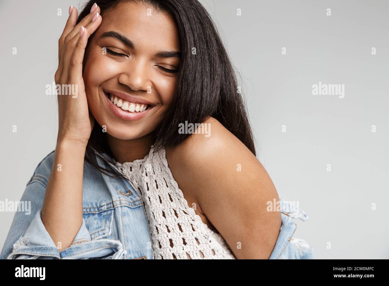 Portrait d'une jeune femme africaine souriante et heureuse avec de longues années cheveux foncés portant des vêtements décontractés se tenant isolé sur fond gris Banque D'Images