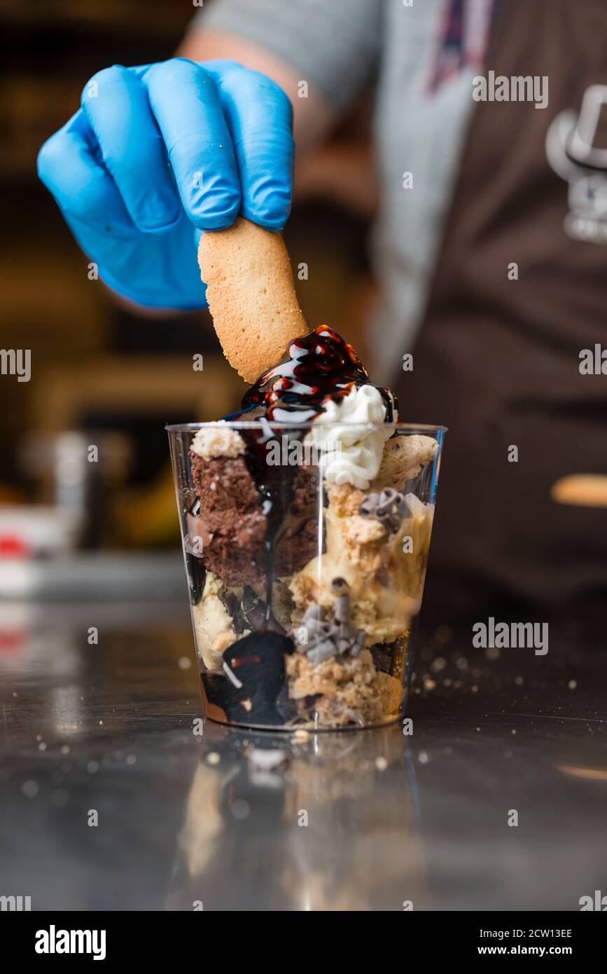 Préparation artisanale d'une tasse de verre de noix et de grains, glace italienne glace glace glace glace à la crème fouettée et biscuits à la langue du chat. Banque D'Images